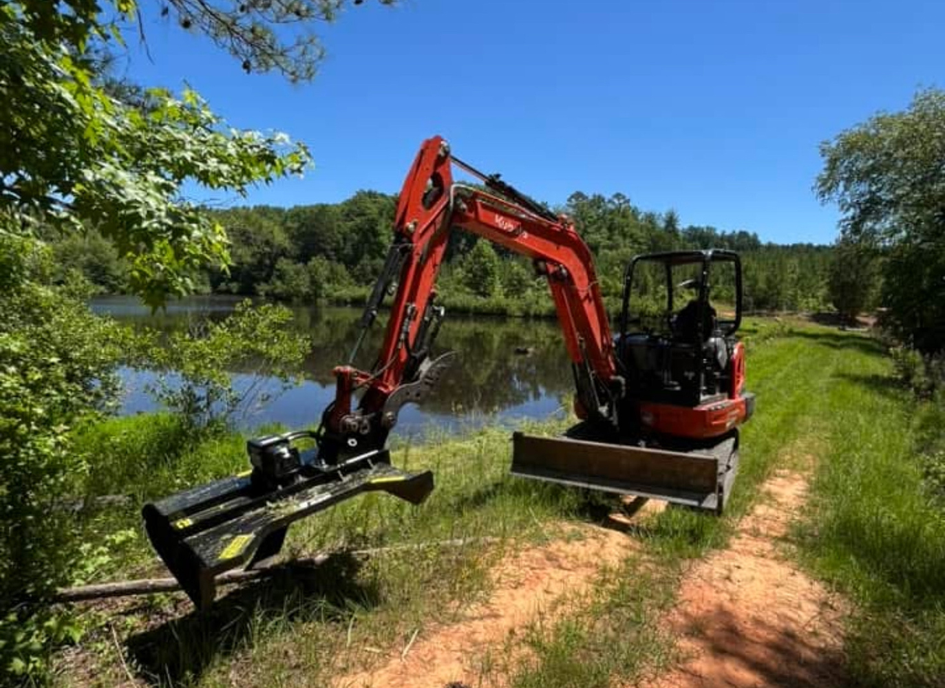 Kubota mini excavator parked near a pond on a red dirt path, ready for edge work