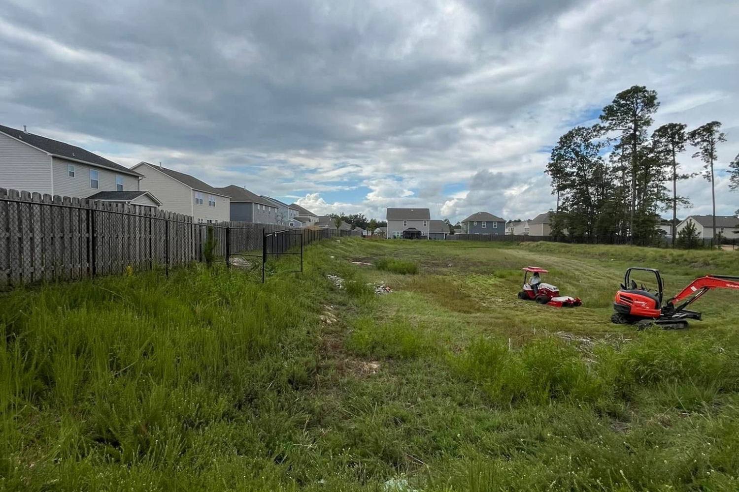 Overgrown drainage path beside a residential fence awaiting clearing and excavation